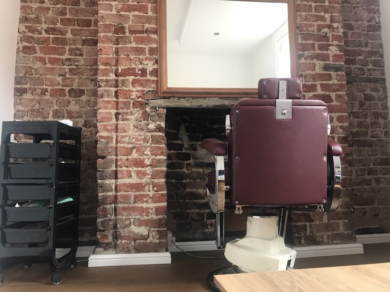 A vintage burgundy leather barber chair against an exposed brick wall inside the salon