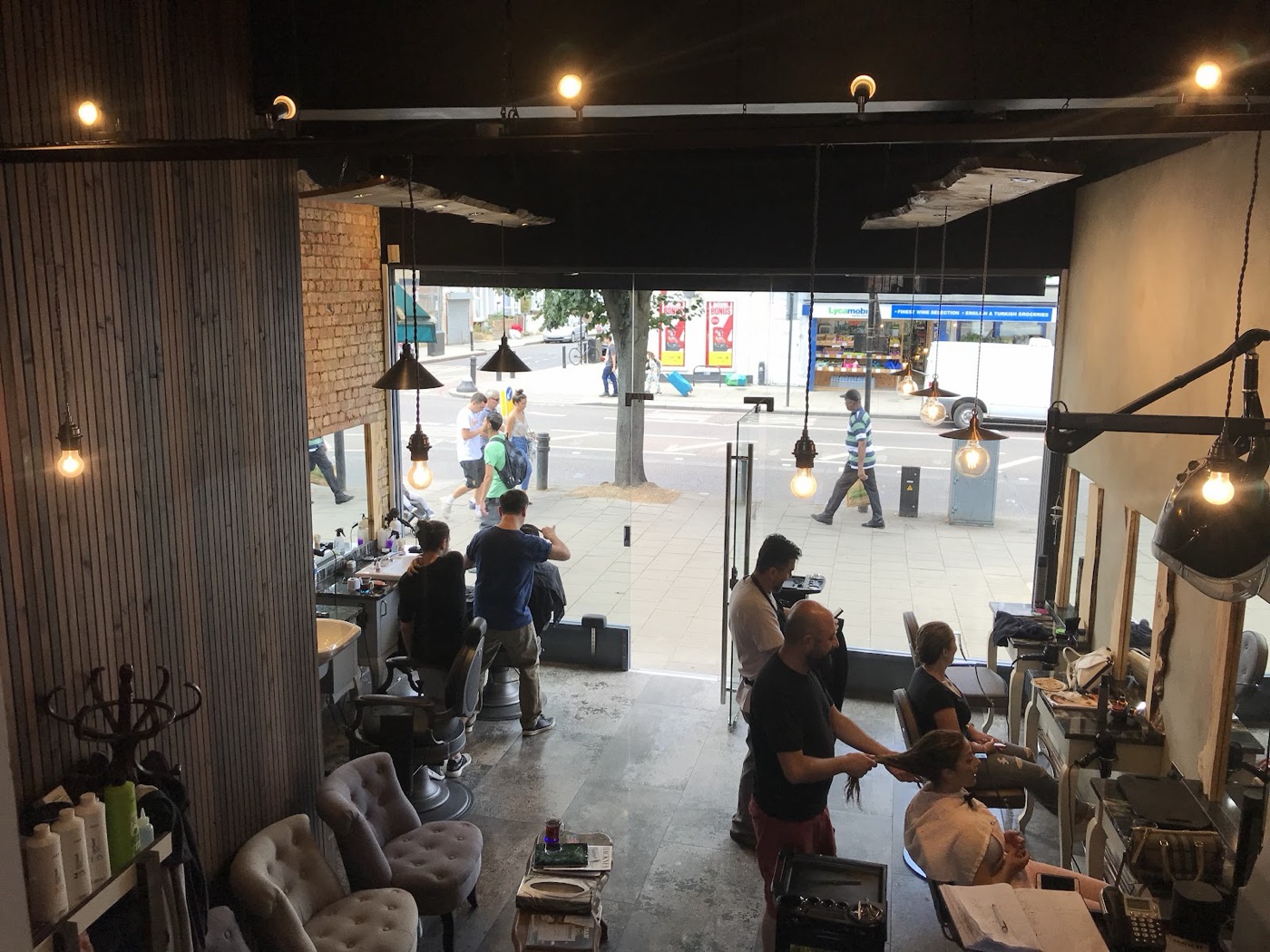 A busy day inside Fantasy Hair Salon, with stylists cutting and finishing hair beneath brass pendant lights and the open shopfront onto Stoke Newington Road